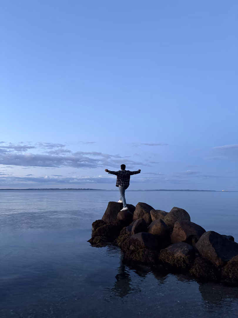 Standing arms-out on a rock breakwater at blue hour in Denmark