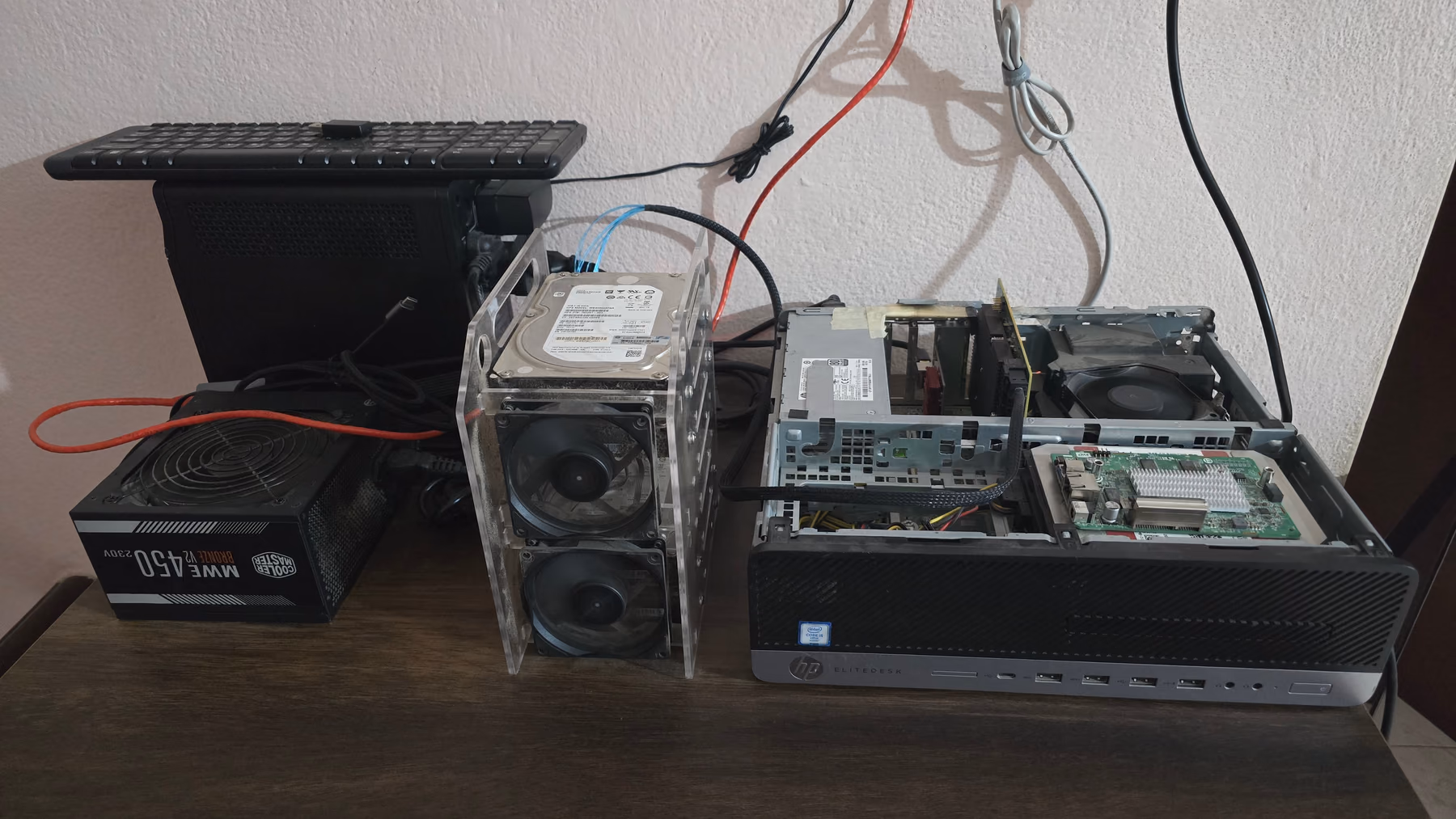 The HP EliteDesk 800 G3 opened on a desk, beside an acrylic rack holding hard drives and a separate power supply